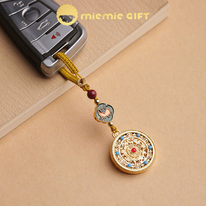 A close-up of the 12 Zodiac Lucky Charm Pendant used as a keychain, attached to a car key. Features an intricate golden alloy spinning disk, a hand-braided cord, vibrant zodiac symbol, and faux cinnabar bead. A stylish and meaningful accessory for luck and prosperity.