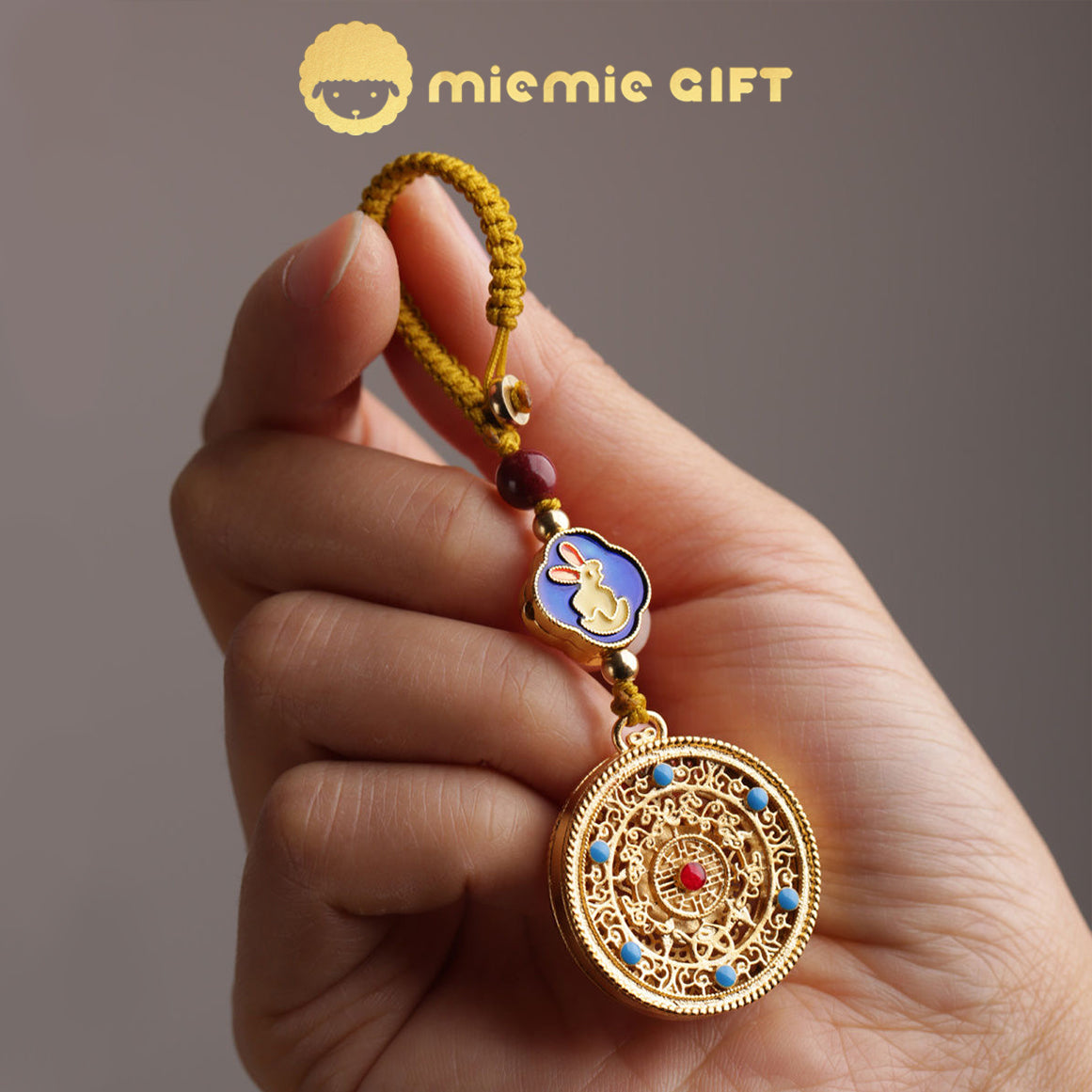 A 12 Zodiac Lucky Charm Pendant being held in hand, showcasing the intricate golden alloy spinning disk, vibrant rabbit zodiac symbol, hand-braided cord, and faux cinnabar bead. A meaningful and portable lucky charm for prosperity and harmony.