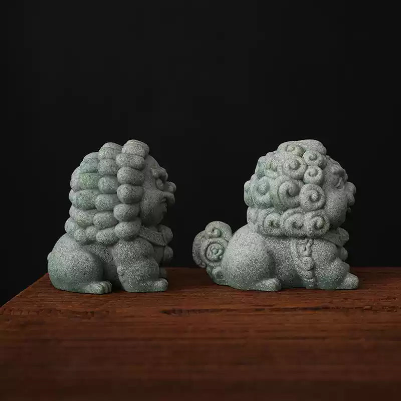 Side view of a pair of green sandstone mini stone lions, showcasing the detailed curly manes and traditional craftsmanship, displayed on a wooden surface.