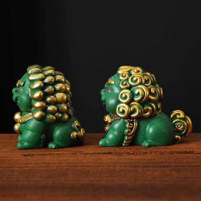 Side view of a pair of green mini stone lions with golden accents, highlighting their detailed manes and tails, symbolizing traditional craftsmanship and prosperity, displayed on a wooden surface.