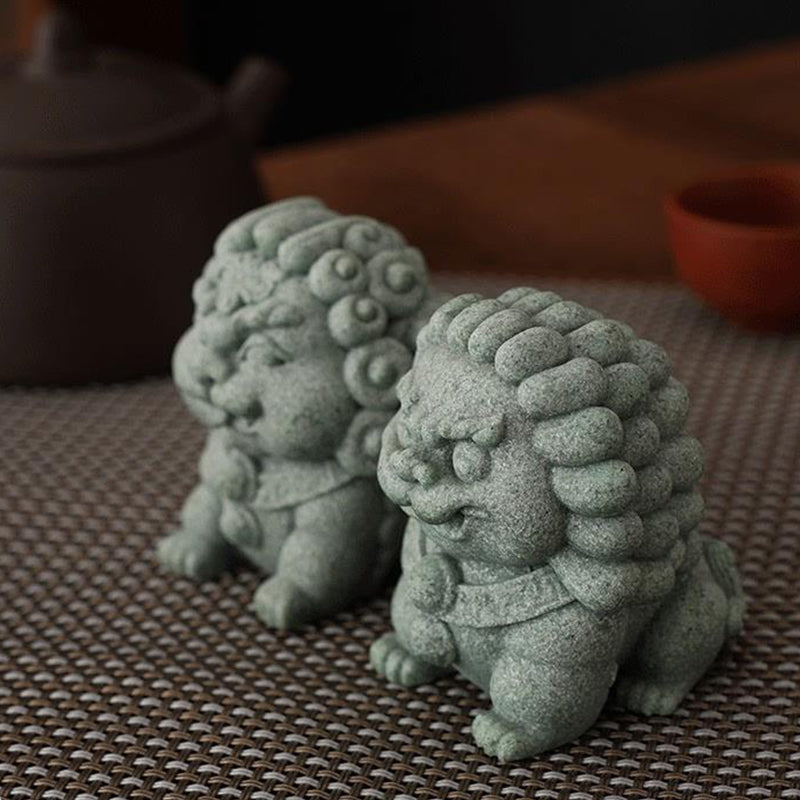 A pair of green sandstone mini stone lions, the Fortune Lion and Peace Lion, displayed on a woven mat with a teapot and cup in the background, evoking a sense of traditional harmony and protection.