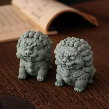 A pair of green mini stone lion ornaments crafted from sandstone, placed on a wooden table. One lion exudes a calm and protective aura, while the other has a fierce and authoritative expression, symbolizing harmony and prosperity in traditional Chinese culture.