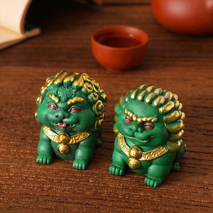 Pair of green Mini Stone Lions with golden accents, symbolizing peace and prosperity, elegantly displayed on a wooden table with a traditional teacup and book in the background.