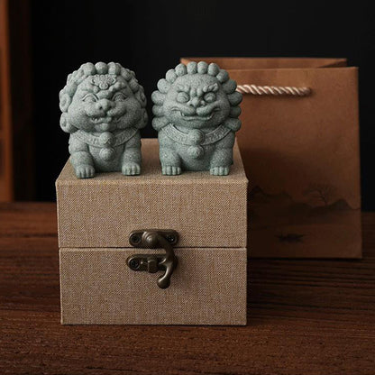 Pair of gray Mini Stone Lions placed on a textured gift box, with a brown gift bag featuring traditional Chinese landscape art in the background, representing protection and harmony.