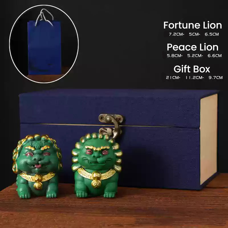 A pair of mini stone lion ornaments, the Fortune Lion and Peace Lion, with intricate golden details, displayed in front of a navy blue gift box and a blue paper bag, showcasing their elegance as a thoughtful gift set.