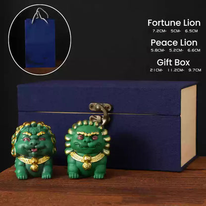 A pair of mini stone lion ornaments, the Fortune Lion and Peace Lion, with intricate golden details, displayed in front of a navy blue gift box and a blue paper bag, showcasing their elegance as a thoughtful gift set.