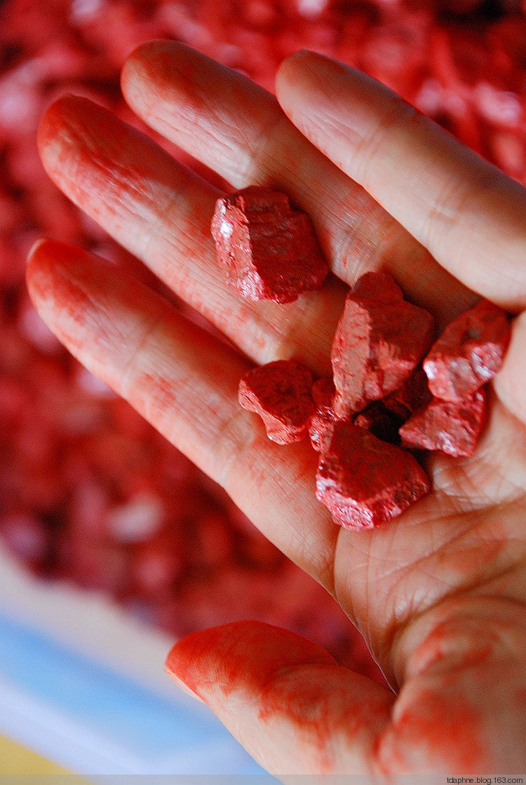 A close-up of natural cinnabar stones held in a hand, showcasing the vibrant red mineral used in creating Taoist Fulu Talismans for its spiritual and protective properties.