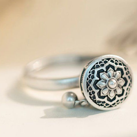 Close-up of a S925 sterling silver rotatable ring featuring an intricate lotus flower design and a small dangling charm, symbolizing mindfulness and blessings.