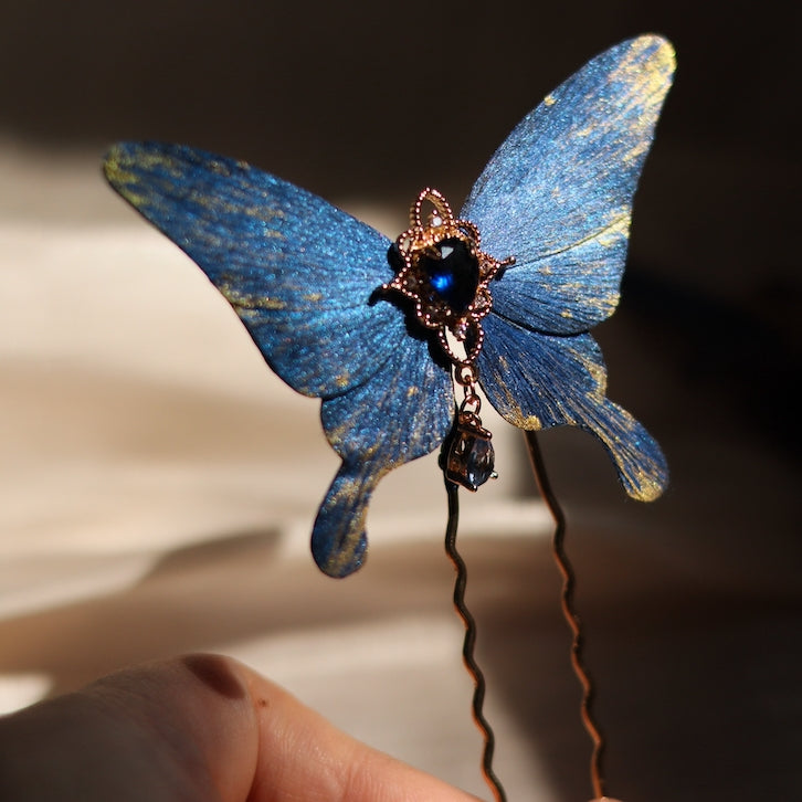 A stunning deep blue butterfly hairpin handcrafted by Chujiu Mountain Atelier, adorned with a sparkling blue crystal centerpiece, golden accents, and a graceful design perfect for elegant occasions.






