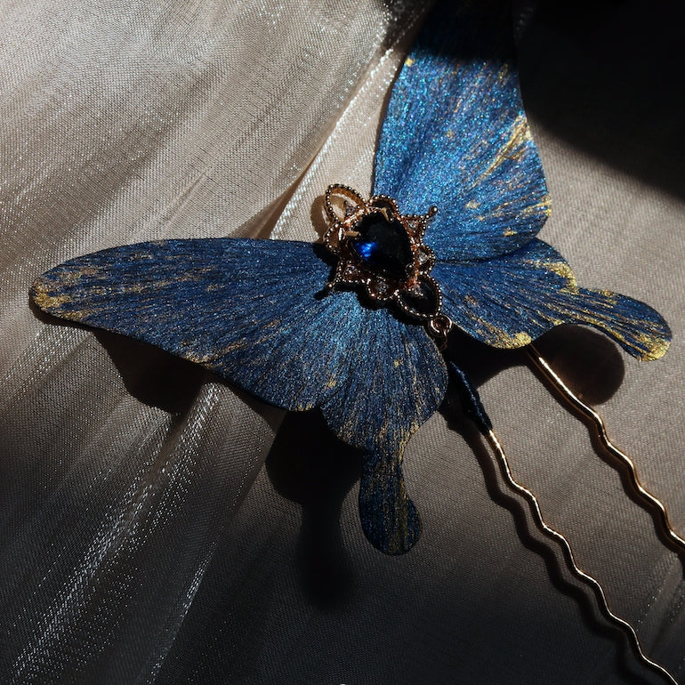 Detailed view of a handcrafted deep ocean blue velvet butterfly hairpin by Chujiu Mountain Atelier, showcasing golden accents, a radiant blue crystal, and shimmering textures inspired by the serene beauty of the sea.