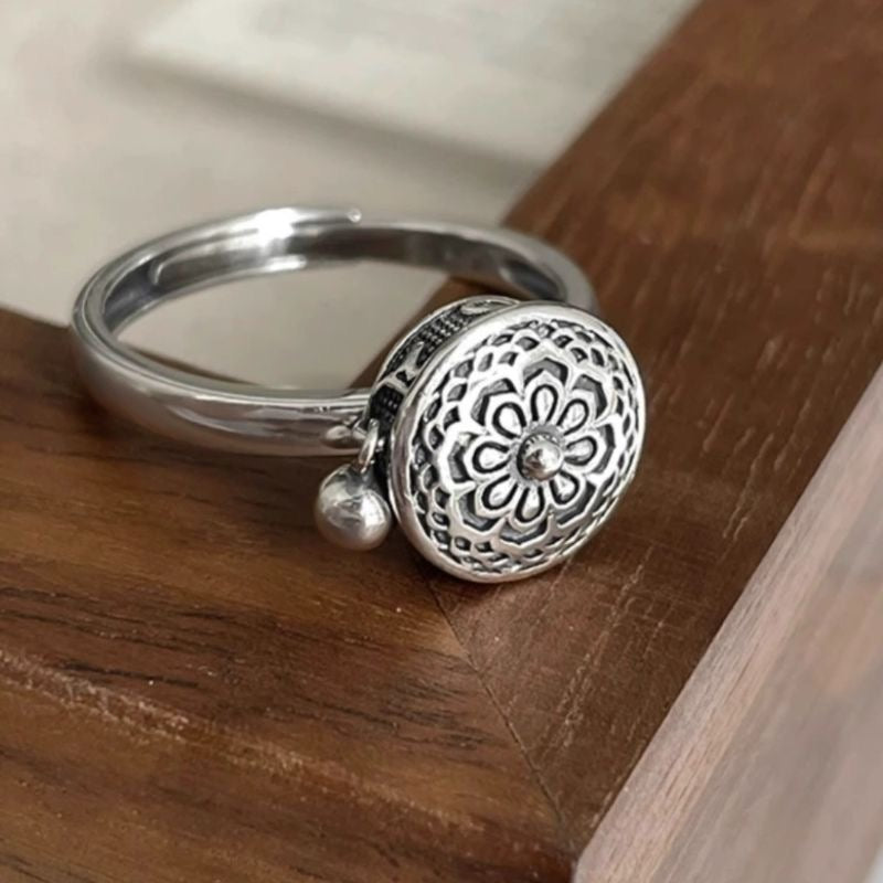 Elegant S925 sterling silver rotatable ring featuring a detailed lotus flower design with a dangling charm, placed on a wooden surface for display.