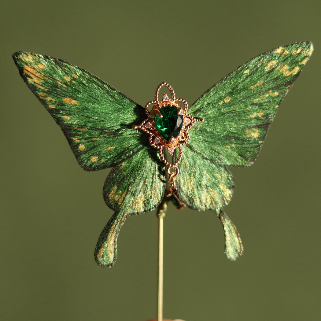 Emerald green velvet butterfly with golden accents and a heart-shaped green crystal at the center, handcrafted by Chujiu Mountain Atelier, available as a brooch, hair clip, or hairpin.