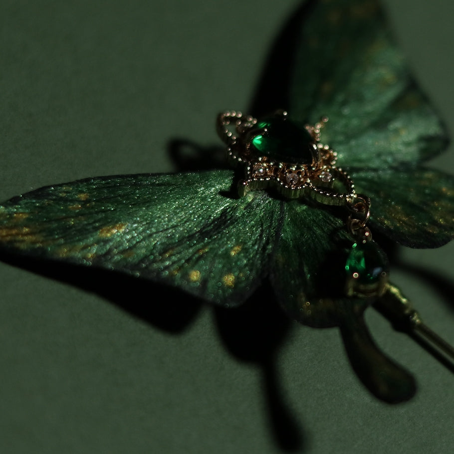 Close-up of a handcrafted emerald green velvet butterfly by Chujiu Mountain Atelier, featuring shimmering golden accents and a heart-shaped green crystal, perfect as a luxurious accessory.