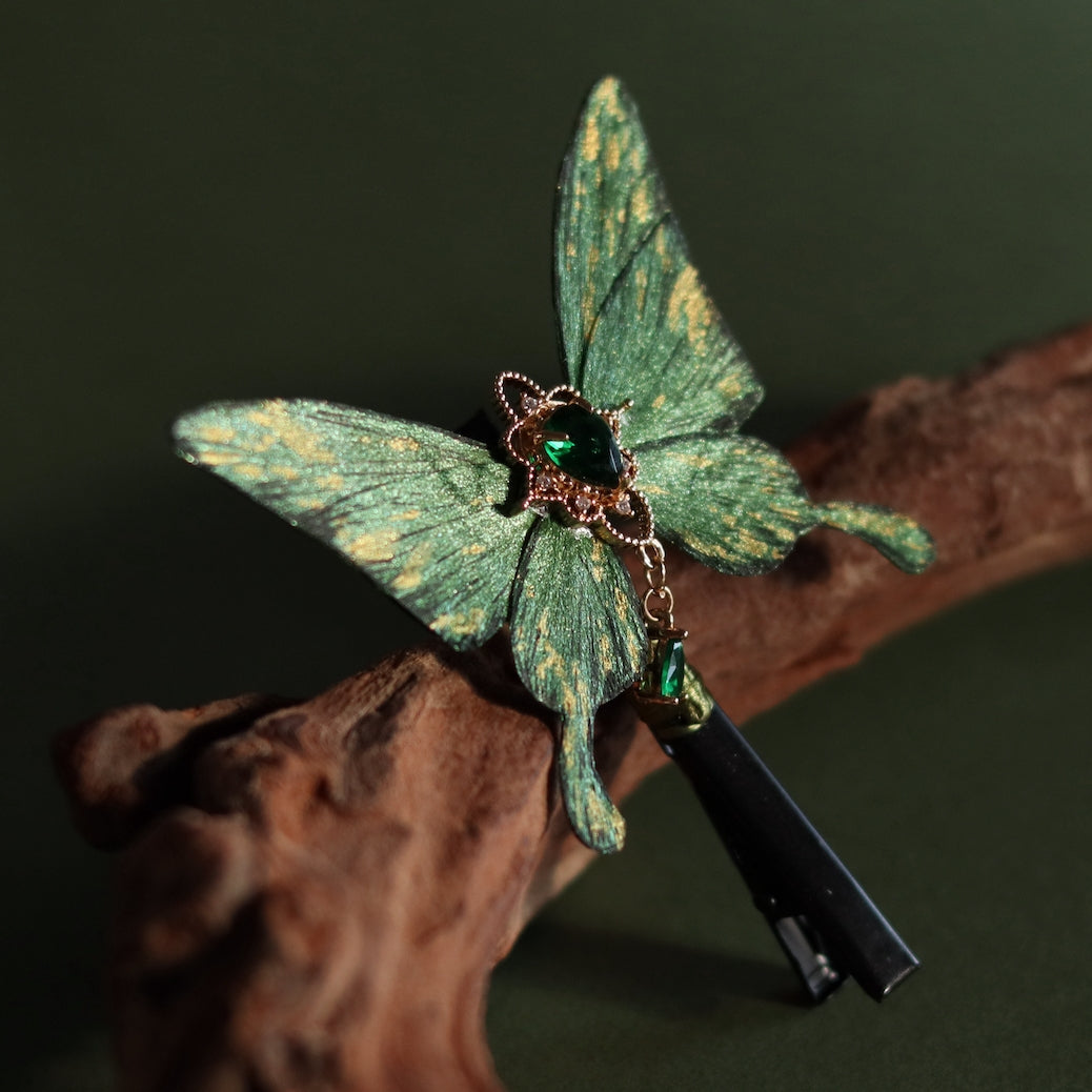 Handcrafted emerald green velvet butterfly hair clip with golden accents and a heart-shaped green crystal at the center, featuring delicate detailing and an elegant tassel, designed by Chujiu Mountain Atelier.