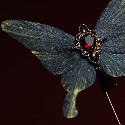 Close-up of a gray butterfly velvet flower hairpin adorned with a vivid red gemstone centerpiece, set against a dark background, emphasizing its intricate craftsmanship.