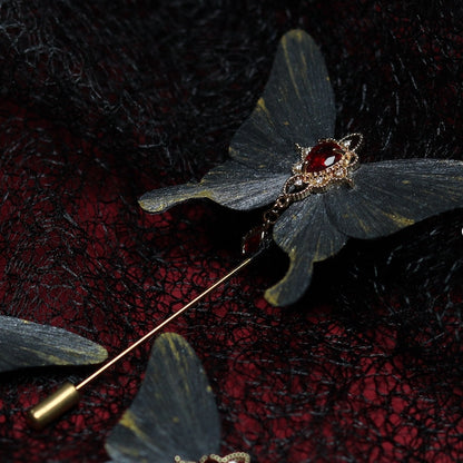 Gray butterfly velvet flower hairpin embellished with a red gemstone and delicate golden details, resting on a textured black lace background with hints of deep red.