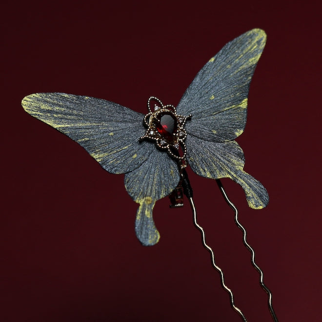 Elegant gray butterfly velvet flower hairpin adorned with a red crystal centerpiece and intricate gold accents, set against a deep red backdrop.