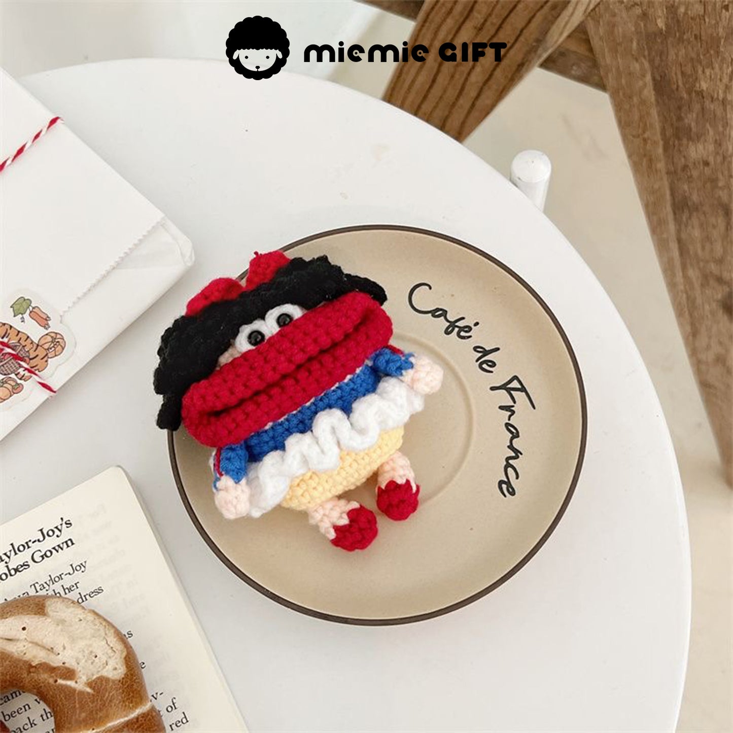 Handcrafted Snow White earphone case in vibrant colors (red, blue, yellow, and white) placed on a café plate. The playful design features black curly hair and a red bow, offering a fun, unique way to protect your AirPods.