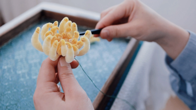 Artisan crafting a yellow velvet chrysanthemum with delicate precision, highlighting the intricate process of traditional velvet flower making.