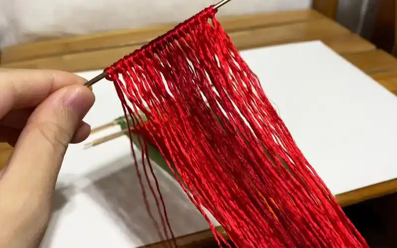 Detailed view of vibrant red silk threads being prepared for traditional velvet flower crafting, showcasing the preparation process.