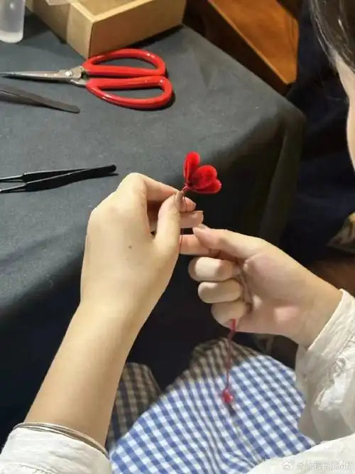 Close-up of a craftsman creating a red velvet heart-shaped flower using delicate hand techniques.