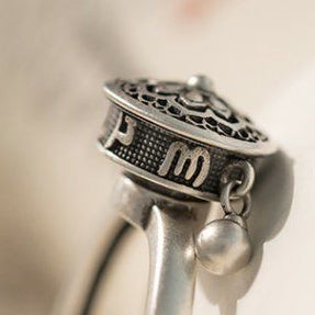 Side view of a S925 sterling silver rotatable ring showcasing engraved Six-Word Mantra symbols and a dangling charm for blessings and mindfulness.