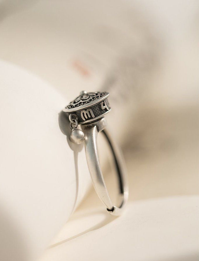 Side view of a S925 sterling silver rotatable ring featuring engraved Six-Word Mantra symbols and a dangling charm, showcasing its intricate craftsmanship.