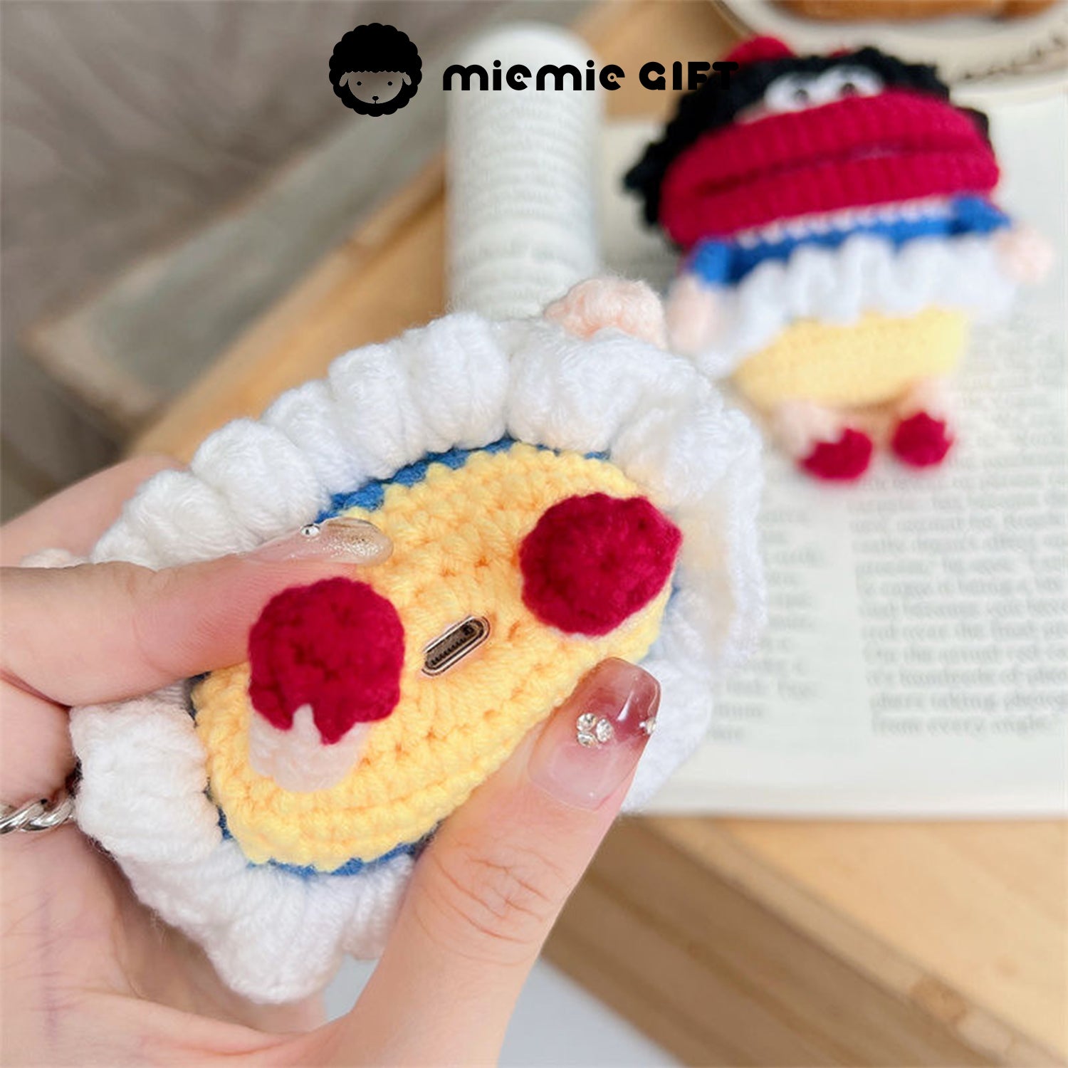 Bottom view of Snow White knit earphone case, showing the colorful yarn design with a yellow base and red details. The case also features an easy-access charging port for your AirPods.