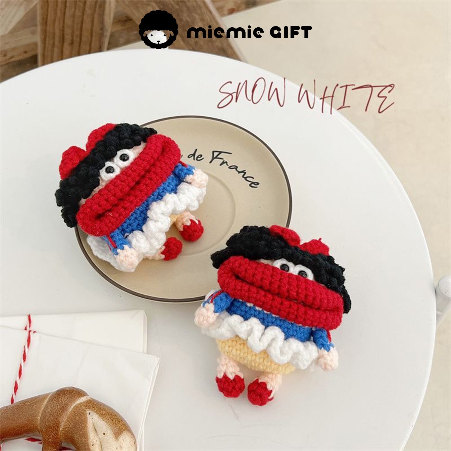 Snow White handcrafted knit earphone case on a plate, featuring vibrant colors in red, blue, yellow, and white. The case has black curly hair and a red bow, offering a playful and unique way to protect your AirPods.