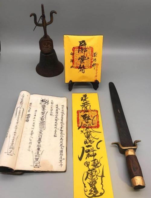 A Taoist Fulu Talisman set including a yellow talisman, ancient scripture book, bronze bell, and ritual sword, showcasing traditional Taoist spiritual tools.

