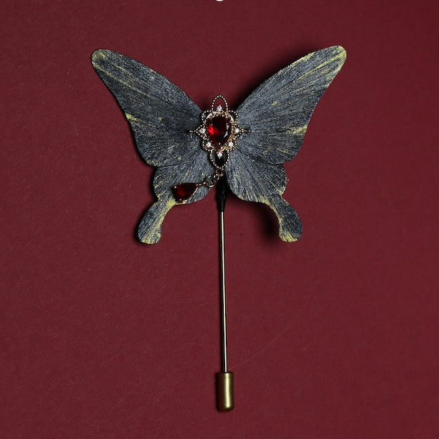 Elegant velvet butterfly brooch with intricate red gemstone details, displayed on a rich crimson background.