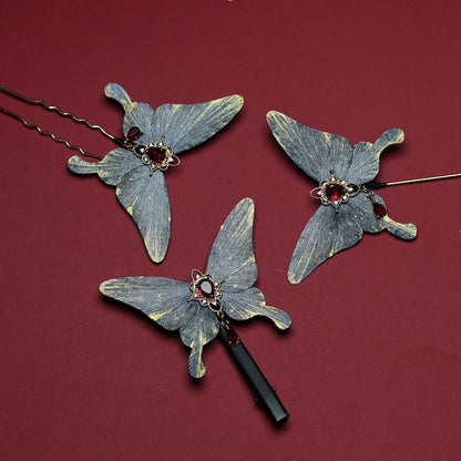 Set of three velvet butterfly hair accessories with intricate red gemstone detailing, displayed on a rich crimson background.