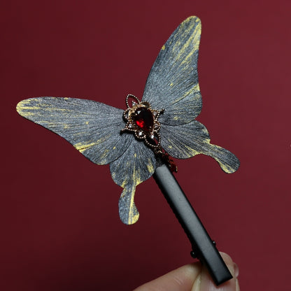 Delicate velvet butterfly hair clip adorned with a radiant red gemstone, showcased on a deep crimson background.