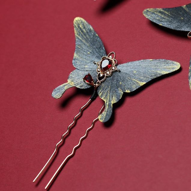 Single velvet butterfly hairpin adorned with a red gemstone centerpiece and delicate gold accents, showcased on a deep crimson backdrop.