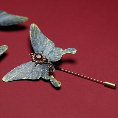 Velvet butterfly lapel pin featuring a red gemstone centerpiece with golden details, beautifully set against a crimson background.